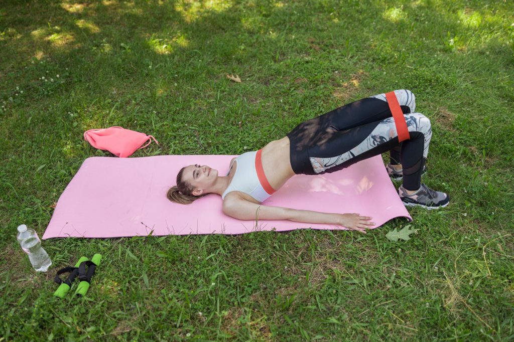 Pretty woman in sportswear does pelvic lift on green lawn grass
